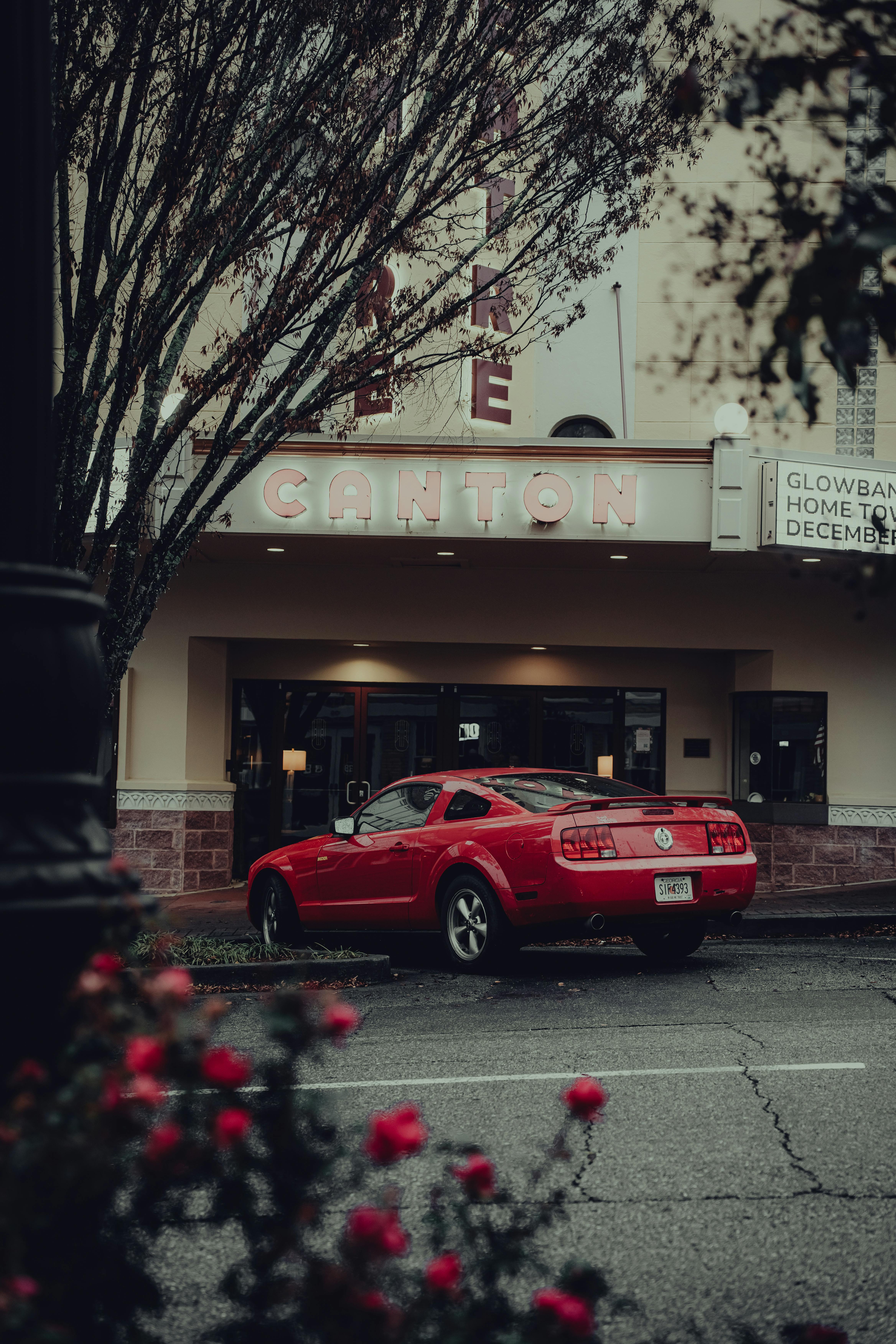 Free A nostalgic scene featuring a classic red car parked outside a vintage theater in Canton. Stock Photo