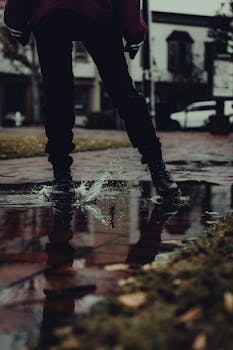 Person splashing in a puddle on a rainy day, urban street scene.