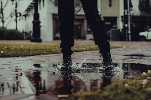 A pair of fashionable boots splashing water on a wet urban street, creating an artistic reflection.