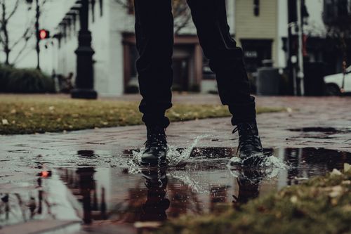 Free A pair of fashionable boots splashing water on a wet urban street, creating an artistic reflection. Stock Photo