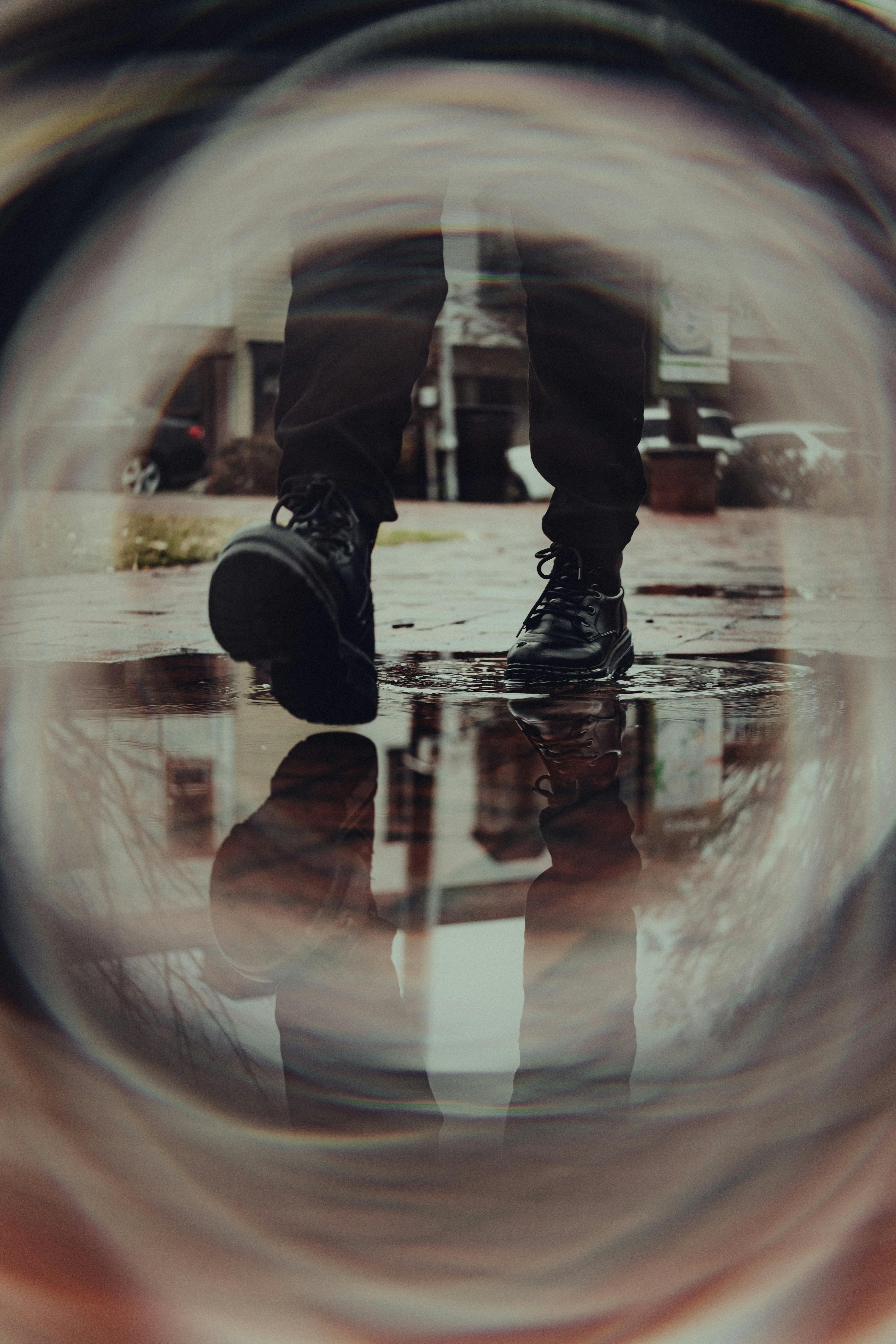 Ücretsiz Yağmurlu bir sokakta bulanık bir lens aracılığıyla yansıyan çizmelerin yaratıcı fotoğrafı. Stok Fotoğraflar