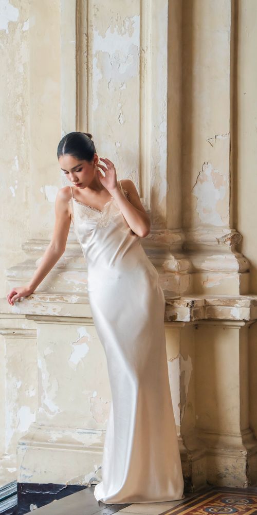Free Elegant woman in a vintage satin gown poses against a textured wall indoors. Stock Photo