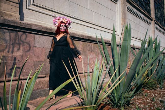 Woman in Day of the Dead attire with floral headpiece near agave plants.
