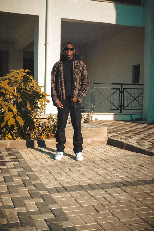 Free Fashionable young man in sunglasses posing confidently outside a modern building, bathed in sunlight. Stock Photo
