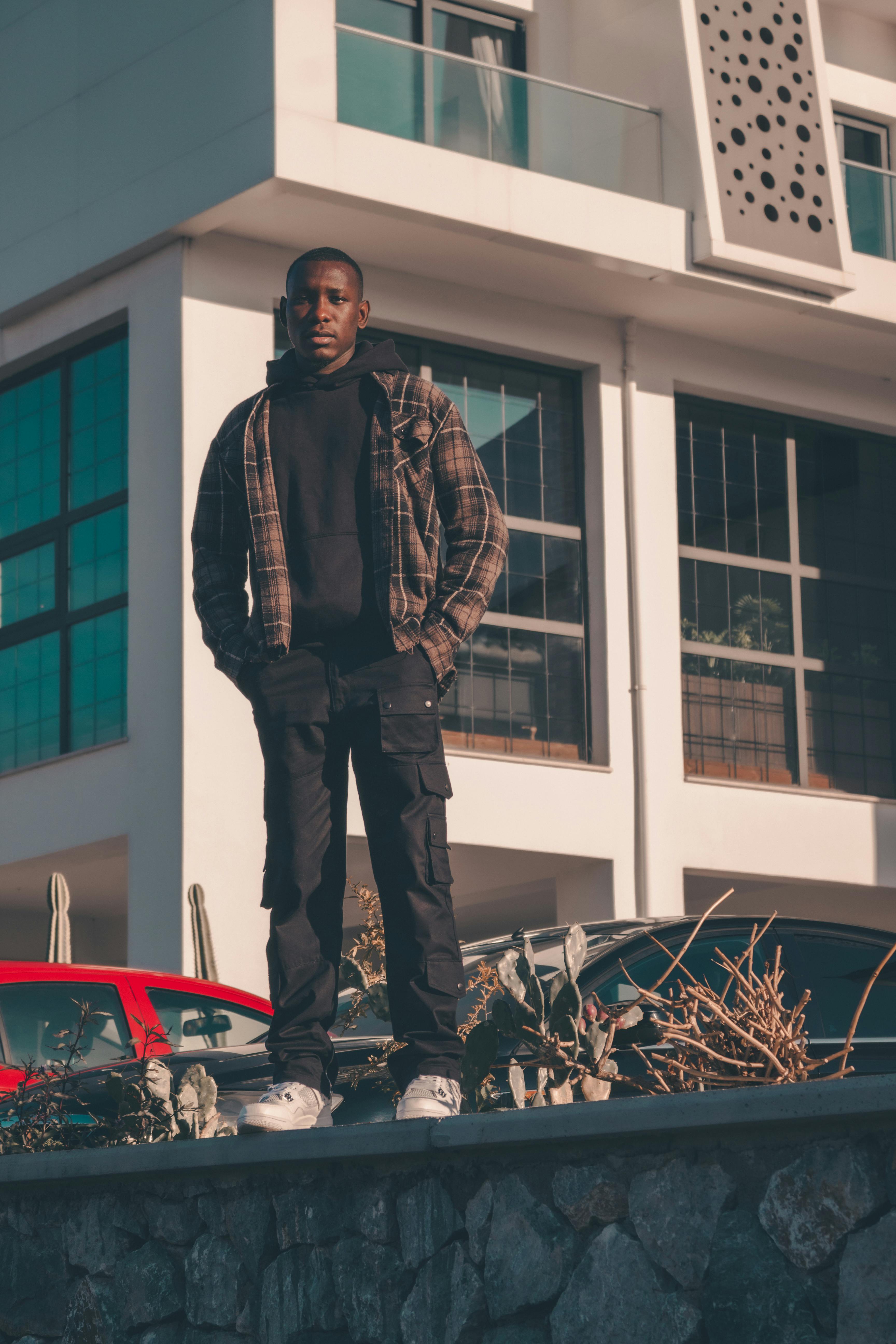 Young man in casual attire standing outdoors in front of modern building, showcasing urban fashion.