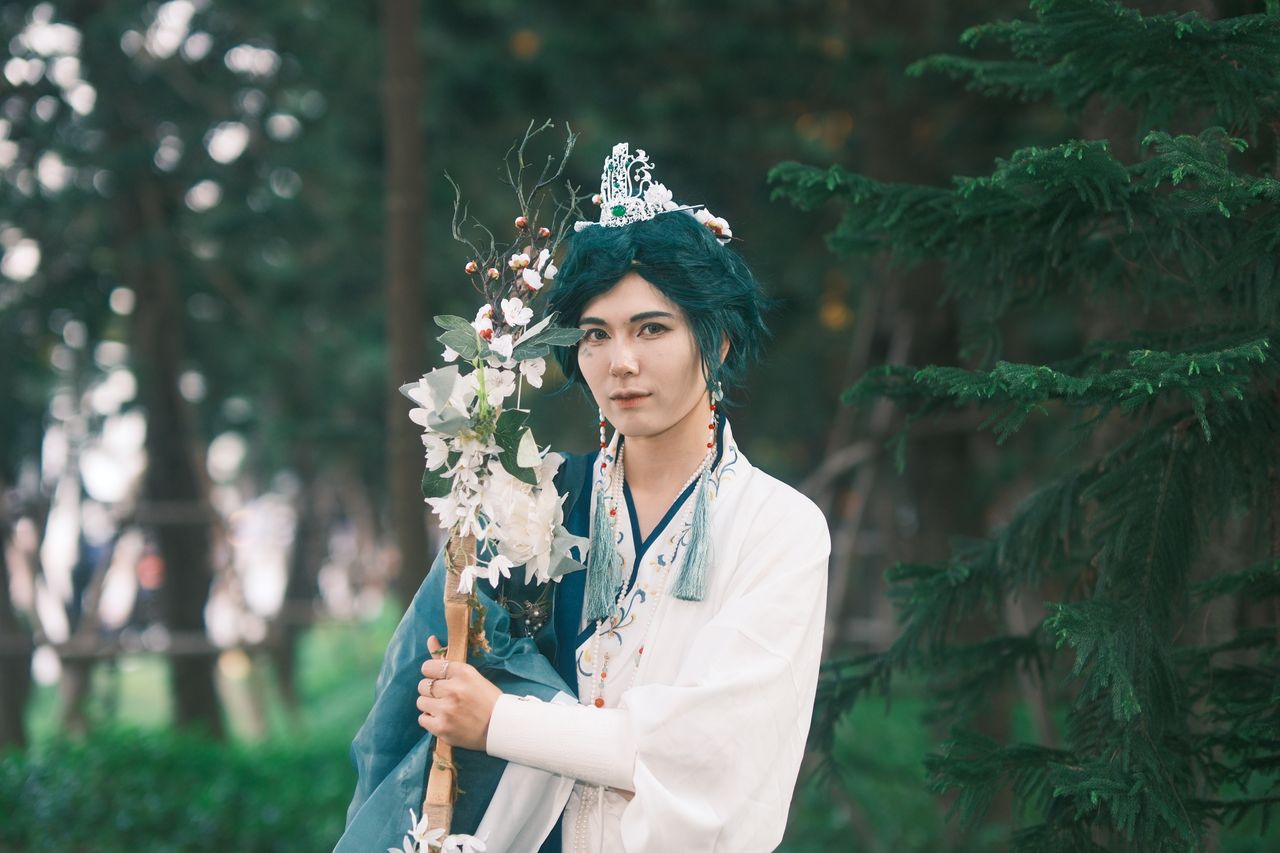 cosplayer in traditional attire holding a floral staff set against a f