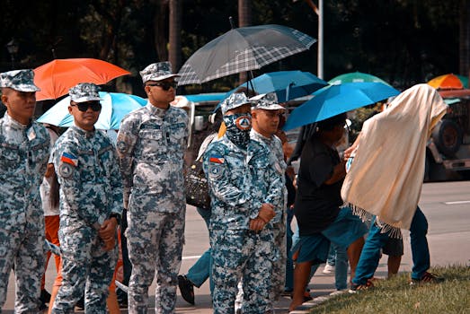 Military personnel stand with umbrellas in a street, showing resilience during a rainy event.