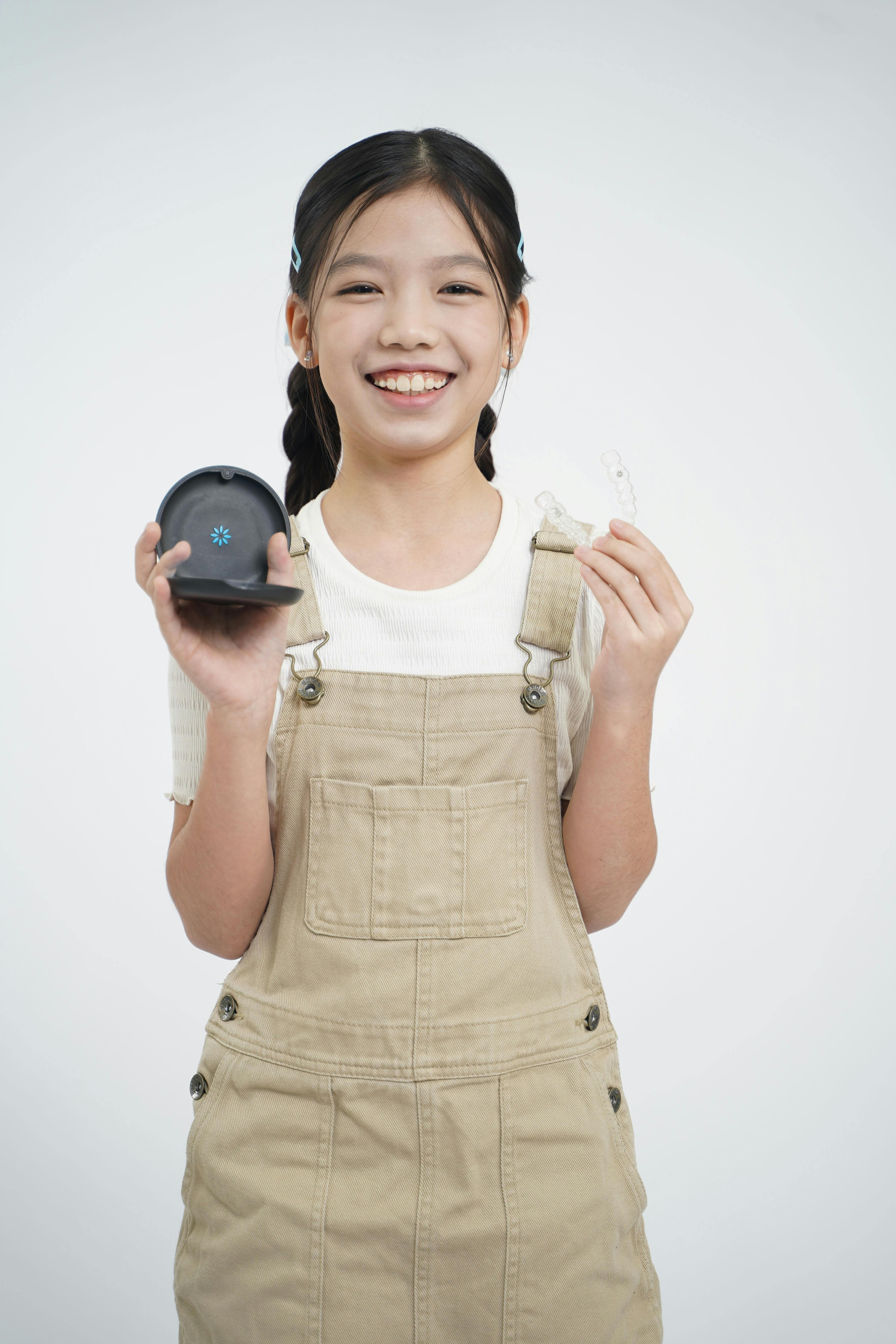 Kostnadsfria Ung flicka ler medan hon håller en tandretainer och dess etui, vilket symboliserar tandvård. Stock foto
