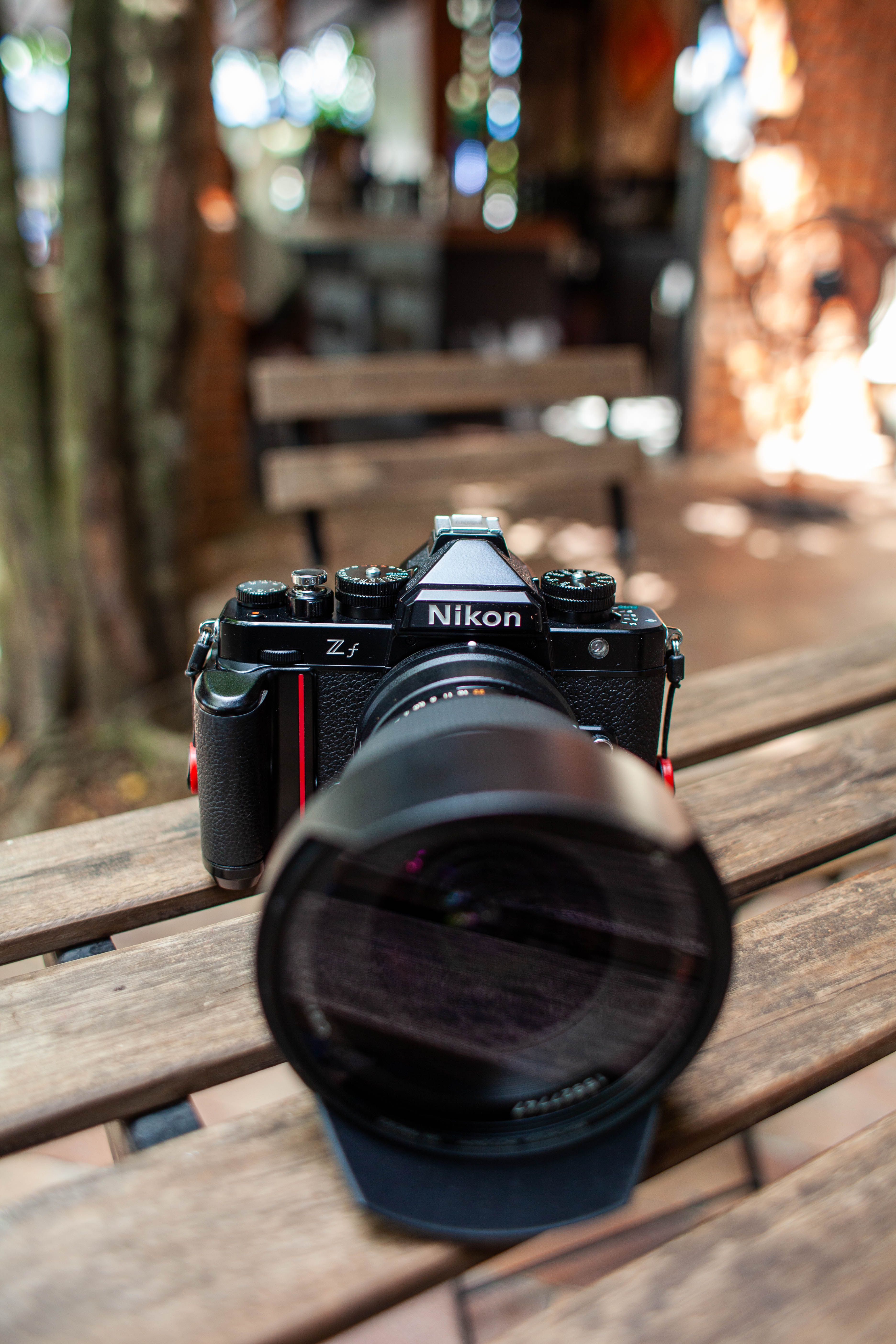 A Nikon camera rests on a wooden table in an outdoor setting, creating a photography-focused scene.