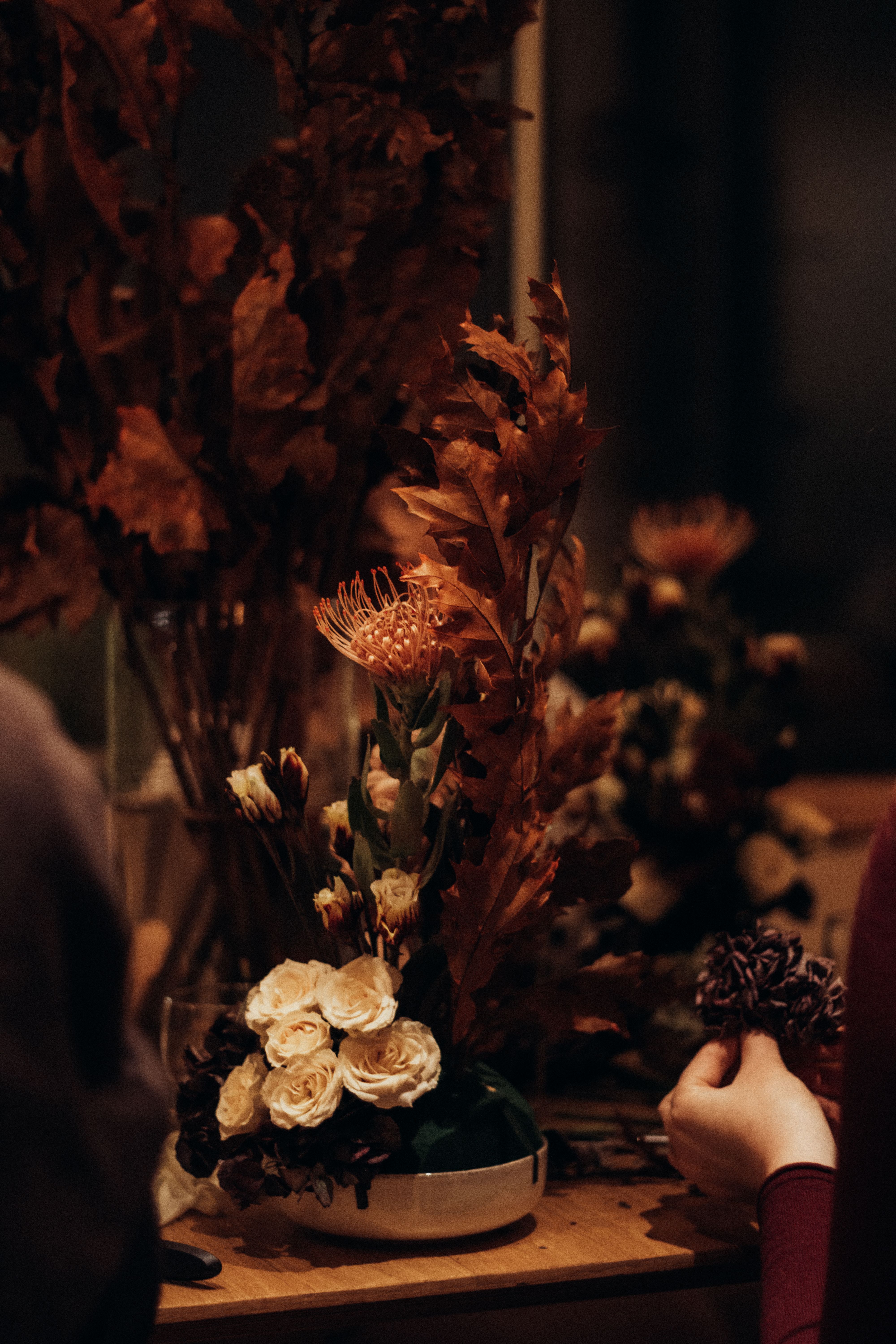 Warm-toned autumn flower arrangement with hands in dim lighting, perfect for seasonal decor.