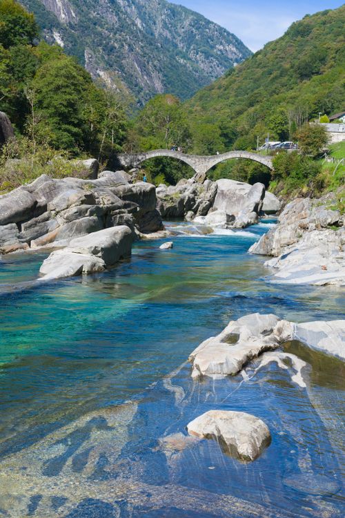 Free Picturesque view of the stone bridge over crystal-clear Verzasca River in Switzerland with lush mountains. Stock Photo