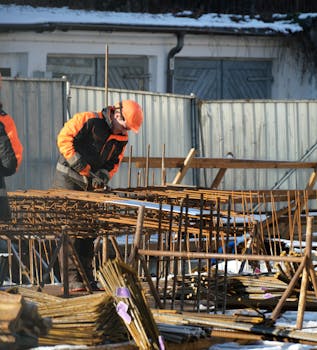 Workers in protective gear handling rebar at snowy construction site in Gdańsk.