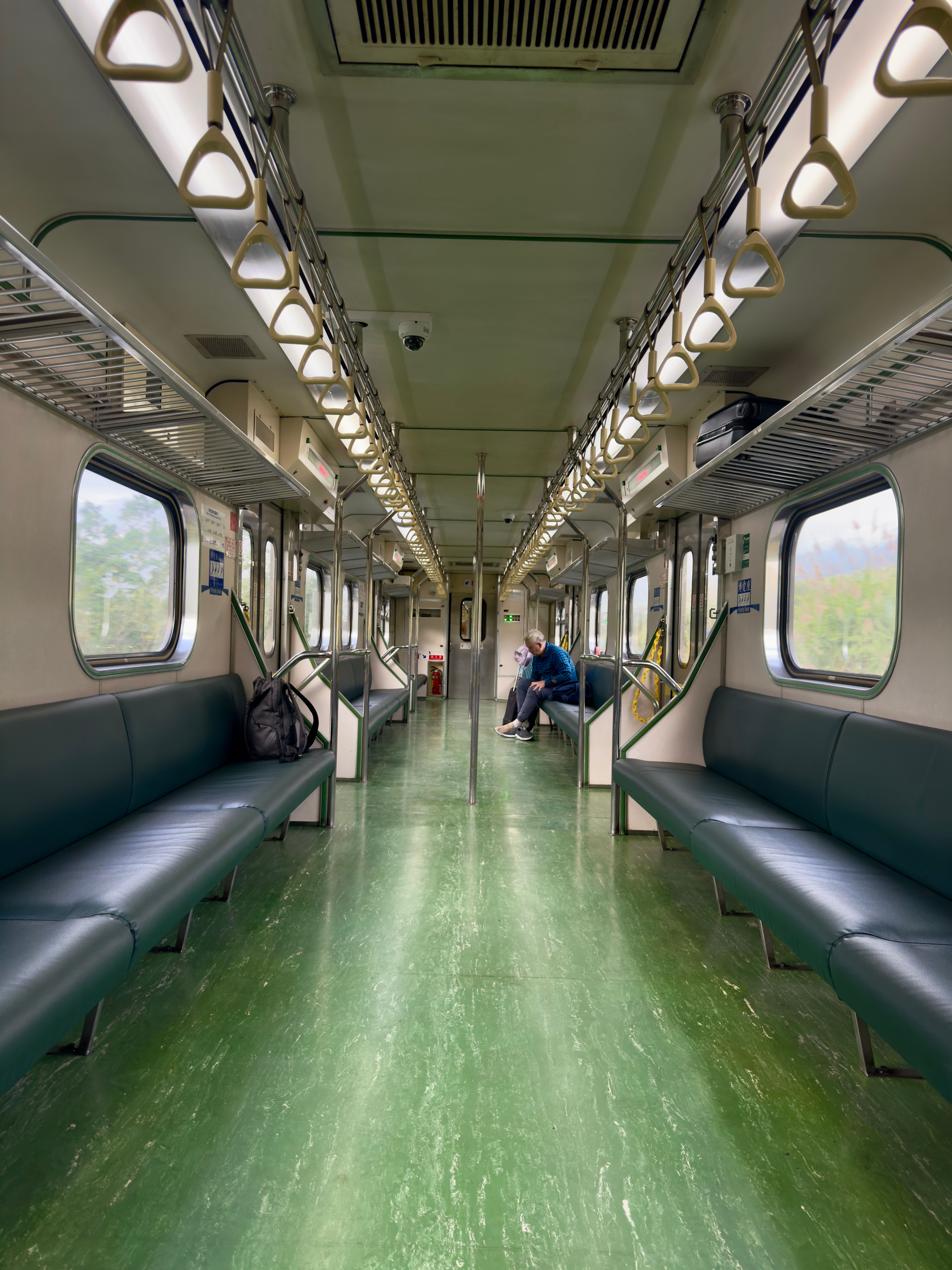 Empty train carriage interior with a lone passenger sitting, offering a peaceful travel scene.