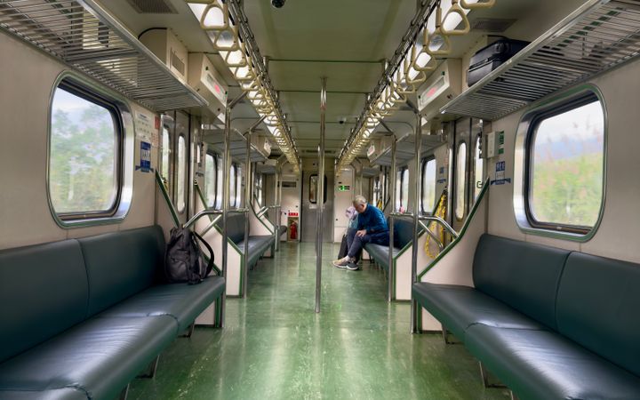 Empty train carriage interior with a lone passenger sitting, offering a peaceful travel scene.