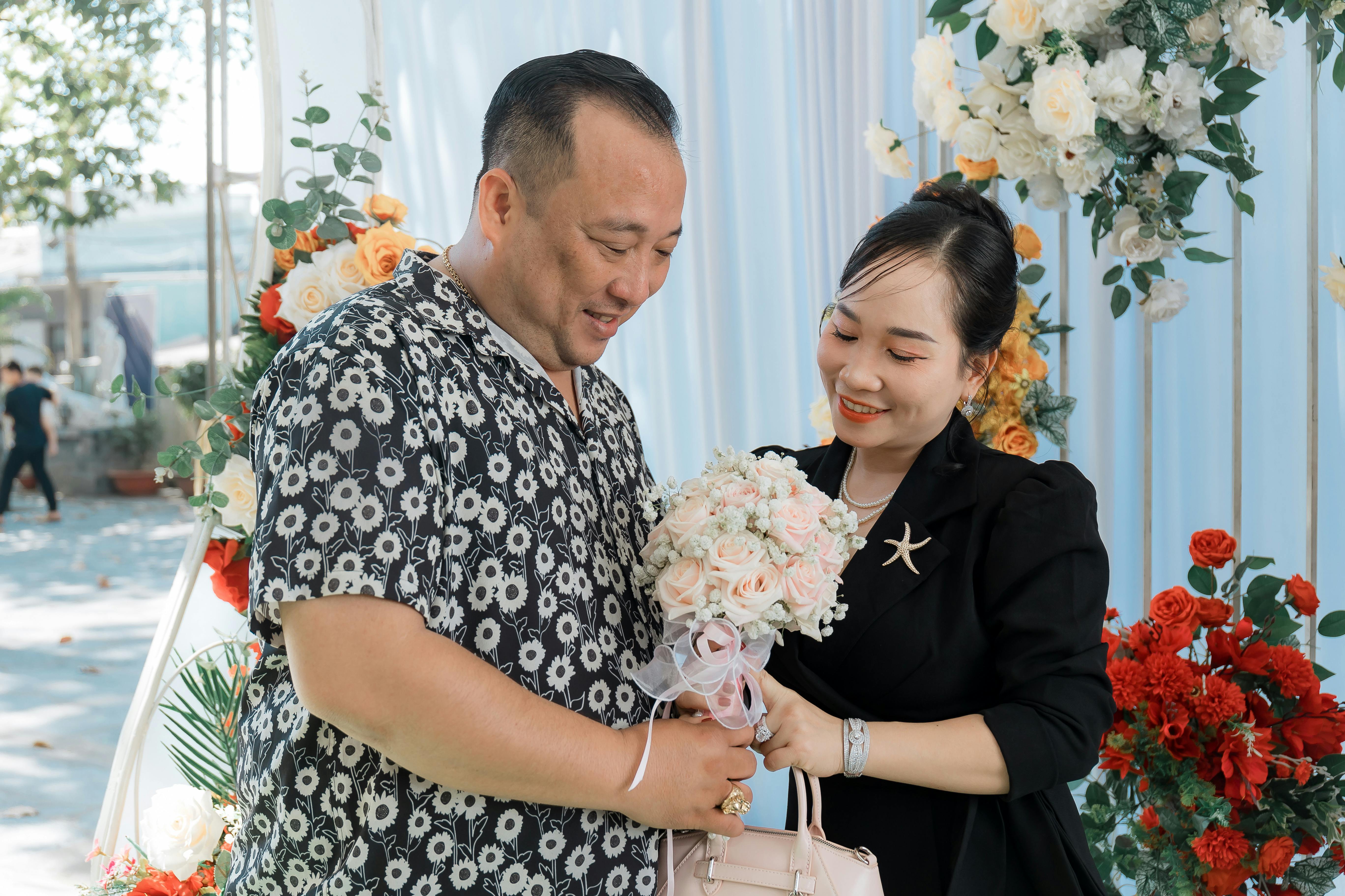 A joyful couple exchanging flowers amidst beautiful floral decorations outdoors.