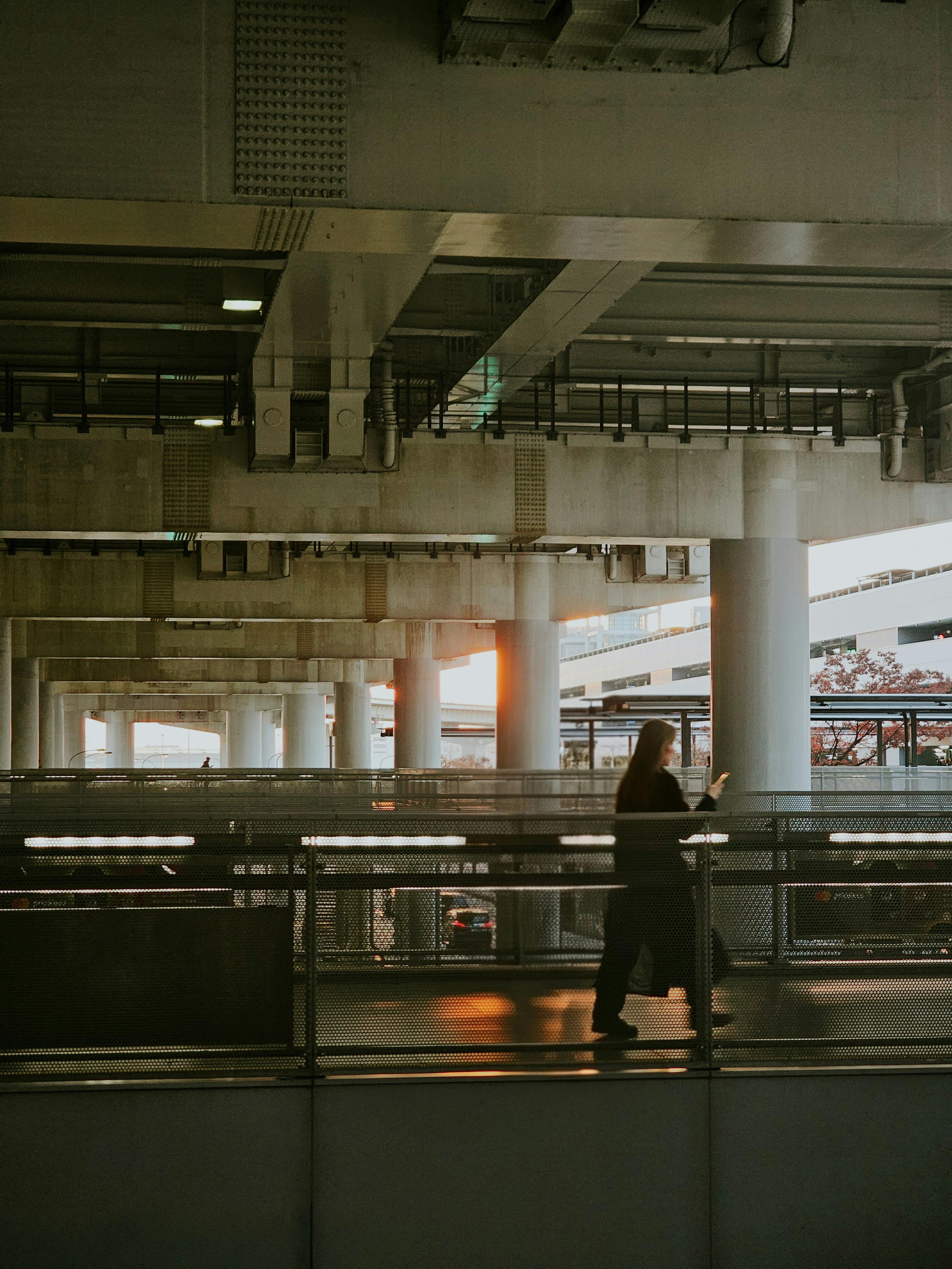 grátis Silhueta de uma pessoa caminhando em uma estrutura urbana industrial sob a suave luz do pôr do sol. Foto profissional