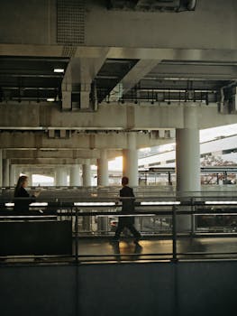 Silhouettes of people walking in an industrial setting at sunset, highlighting urban lifestyle and architecture.