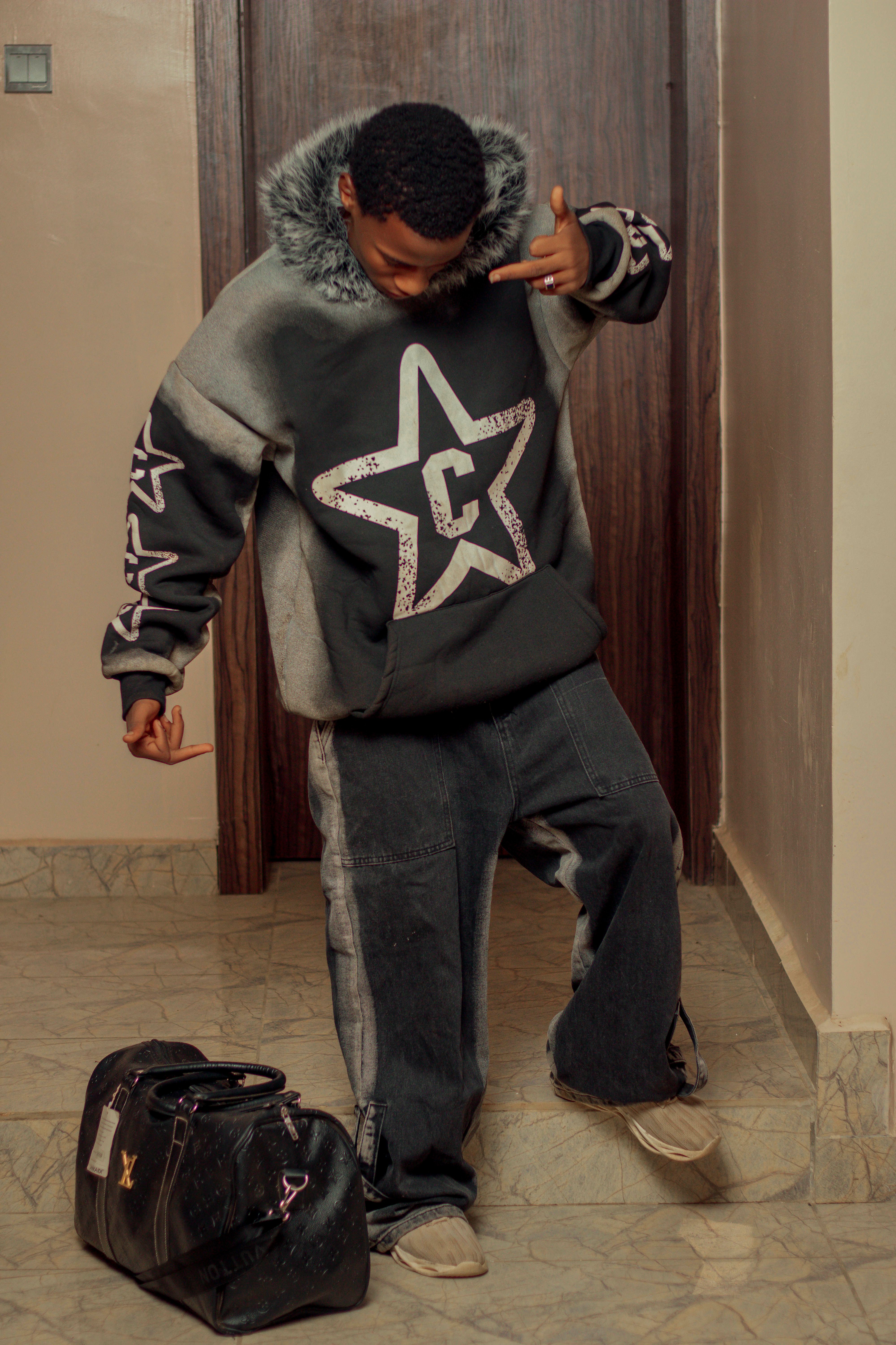 A trendy teenager in a star-patterned hoodie poses indoors with a duffle bag.