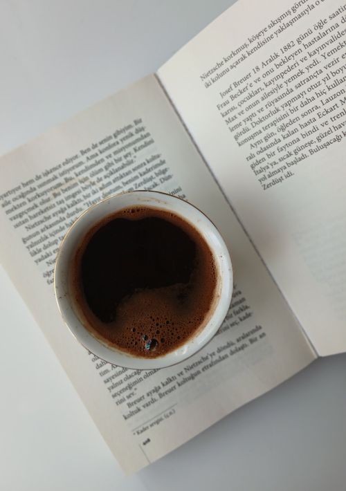 Free Top view of a cup of dark coffee placed on an open book, creating a cozy reading scene. Stock Photo