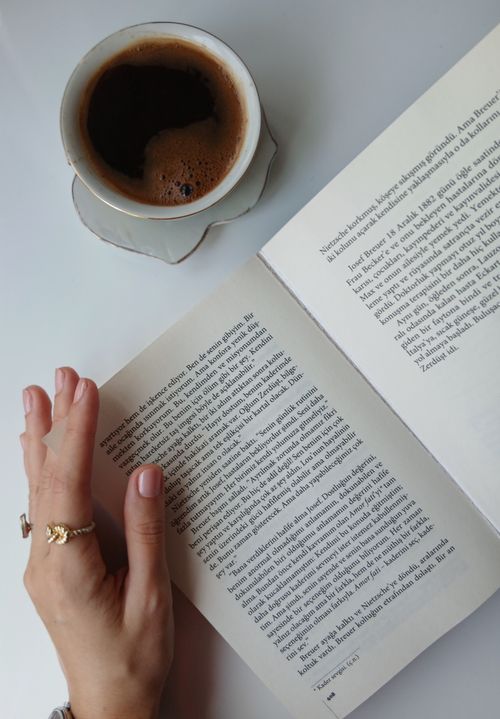 Free Cozy morning scene with coffee and a hand turning book pages on a white table. Stock Photo