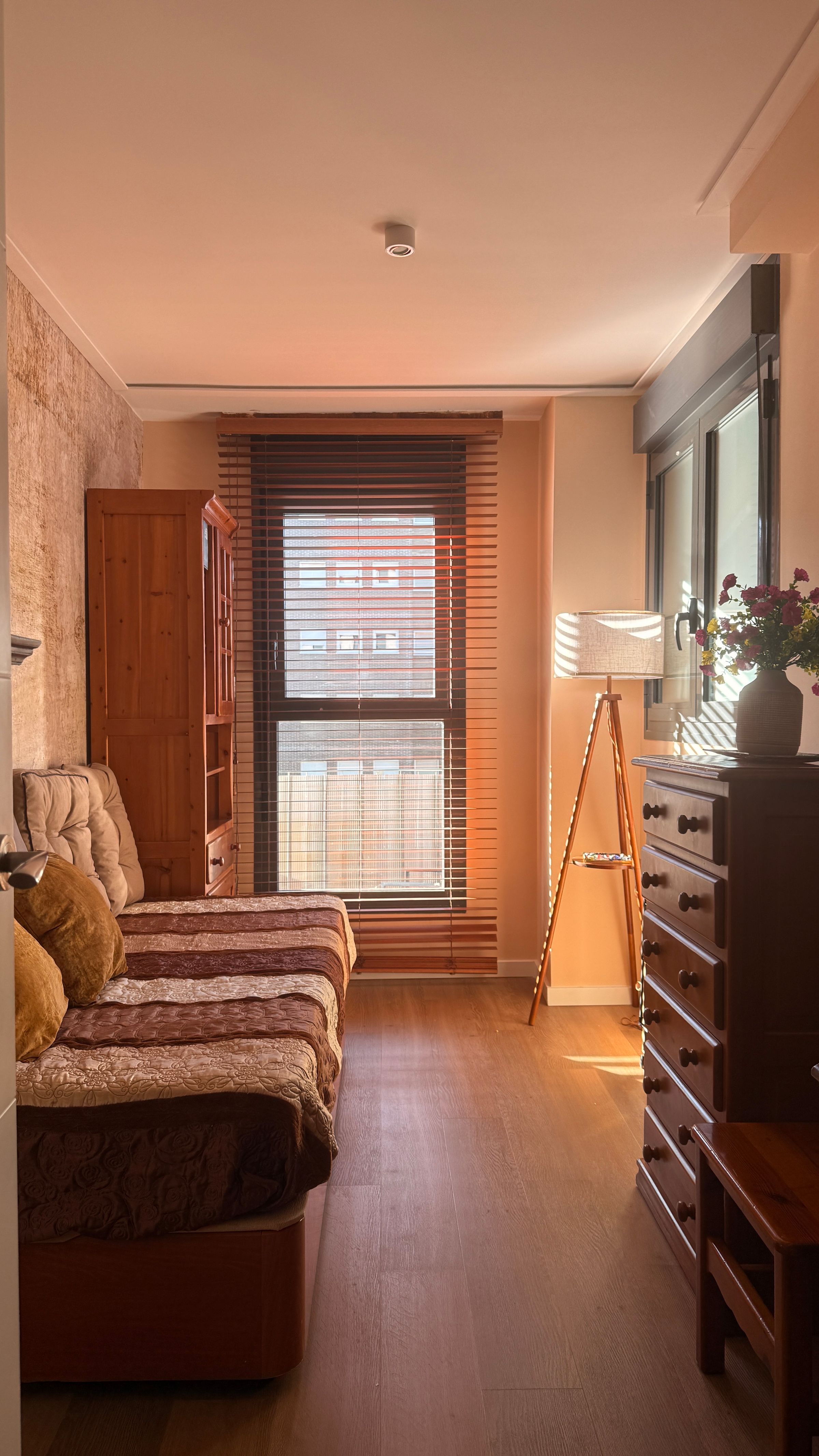 Sunlit bedroom with carved dark-wood furniture, cream upholstery, floral curtains and a warm parquet floor