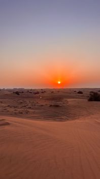 Captivating view of the sun setting over a tranquil desert, casting warm hues across the sand dunes.