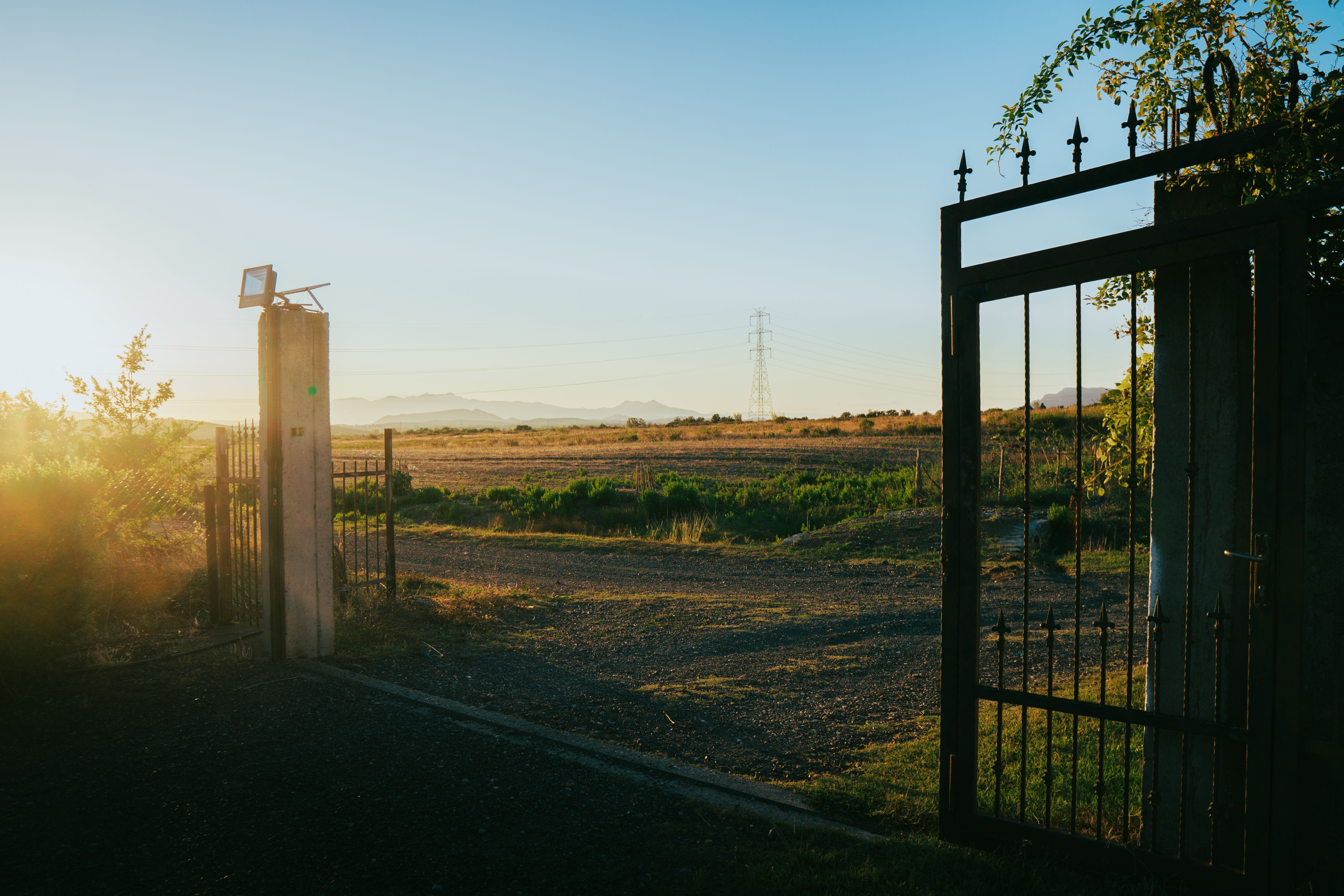 Serene sunset view through an open gate in Fishtë, showcasing the tranquil Albanian countryside.