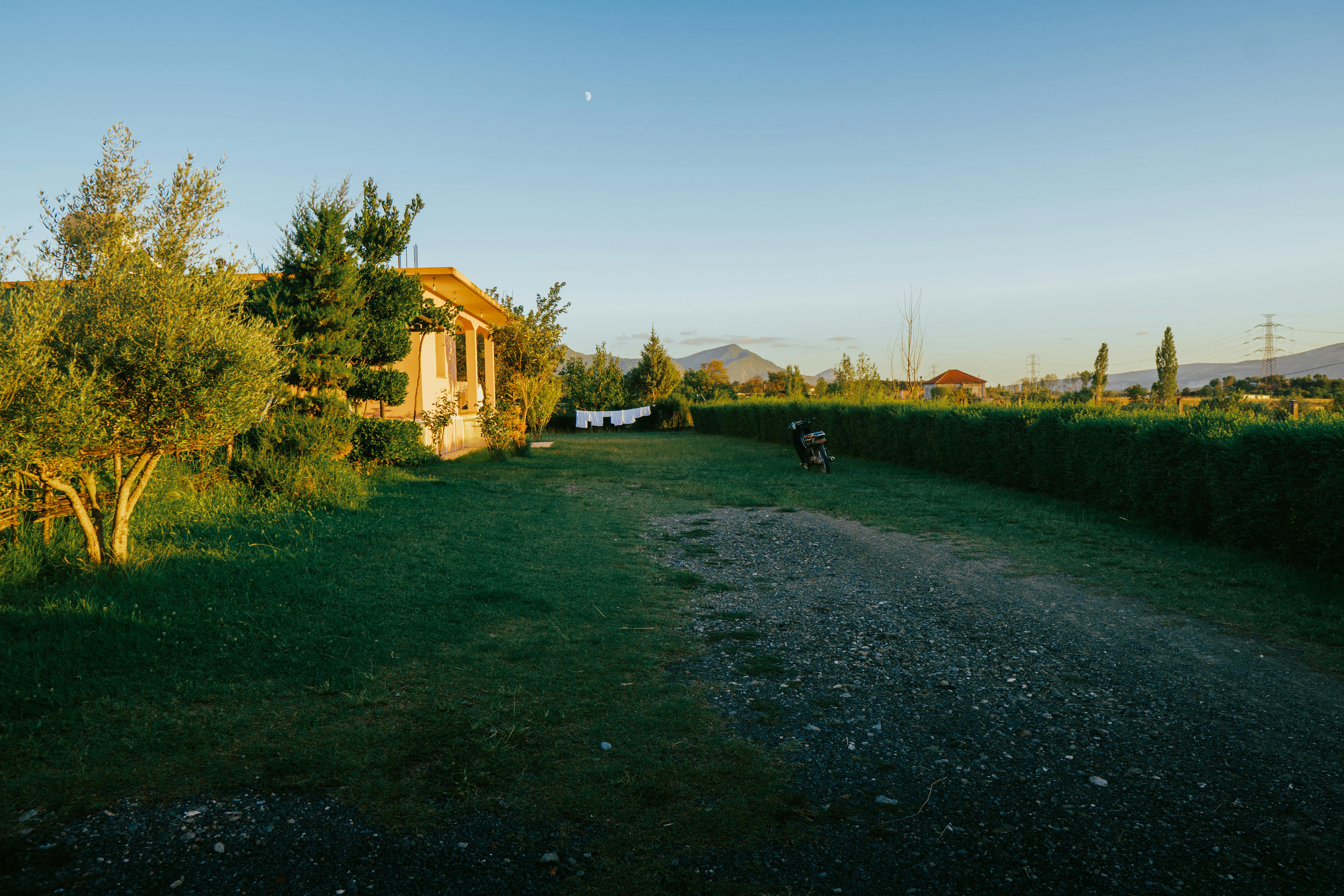 Explore the tranquil Albanian countryside at sunset with lush greenery and distant mountains.