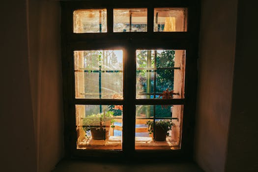Sunset through a rustic window with potted plants in Fishtë, Albania captures serene village charm.
