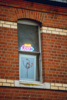 Colorful neon sign with 'We Are Open' text in window of brick building, urban city vibe.
