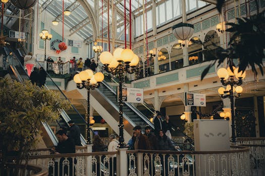 Interior of a vibrant shopping mall with festive holiday decorations and multiple shoppers on escalators.