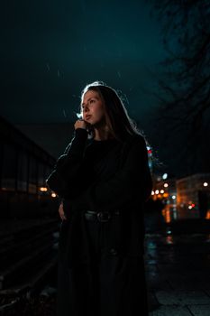 Dramatic portrait of a woman standing under streetlights on a rainy night.
