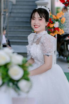 A smiling bride in a beautiful lace wedding dress with floral decor around, exuding elegance and happiness.