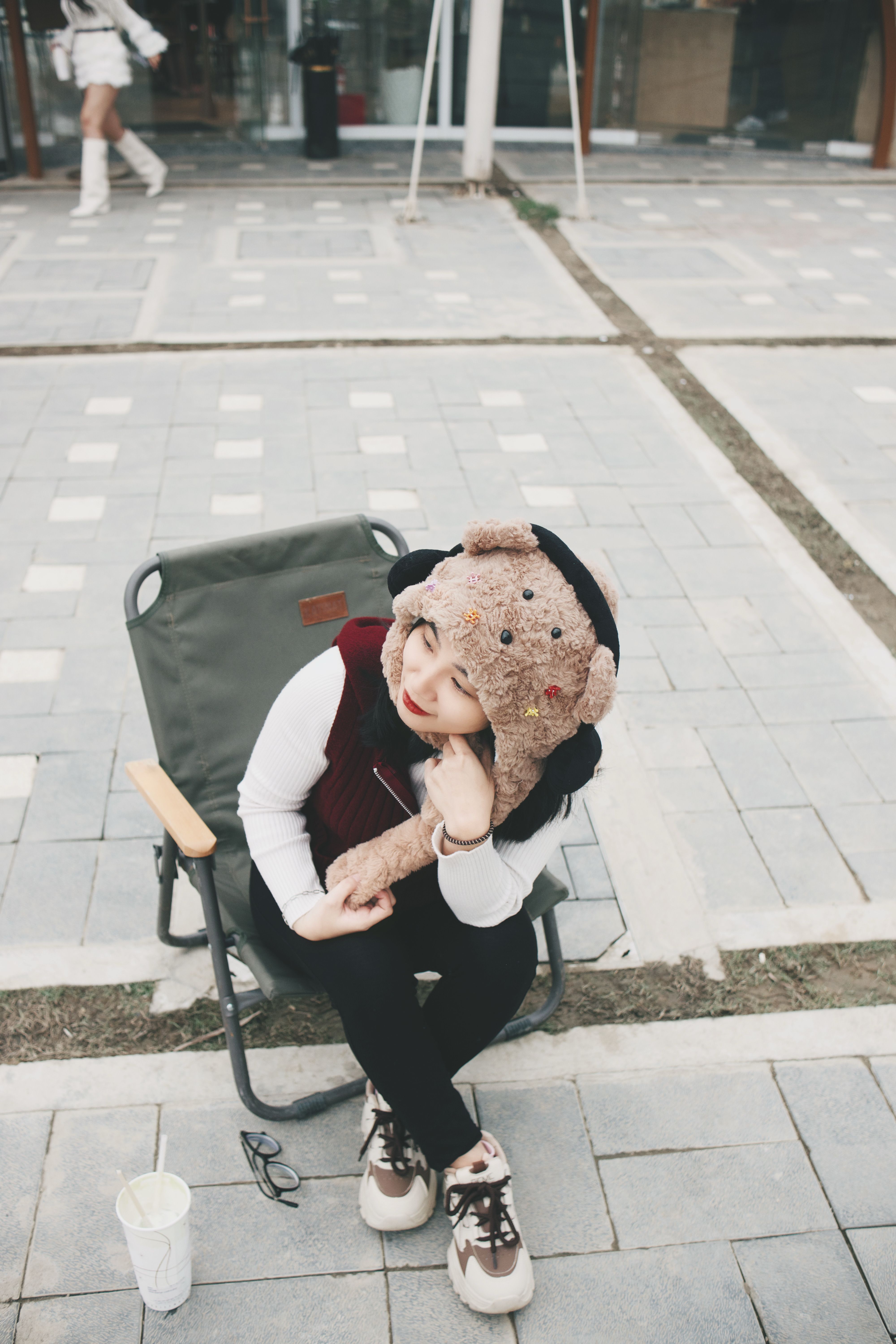 Cheerful woman in bear hat sitting outside on a chair during winter, smiling.