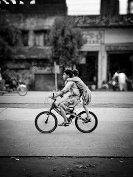 Dynamic street photograph of two children riding a bicycle through an urban landscape.