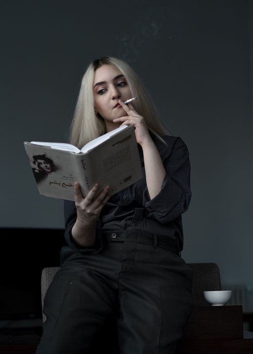 Free A young woman smokes while reading a book, capturing a serene and thoughtful moment. Stock Photo