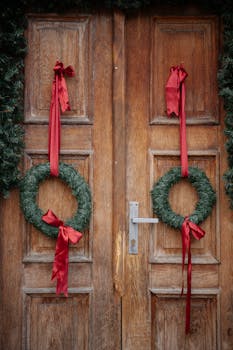 Rustic wooden door adorned with holiday wreaths and red ribbons, evoking Christmas spirit.