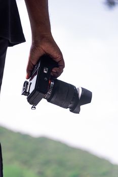 Hand holding a camera against a scenic outdoor backdrop, highlighting photography passion.