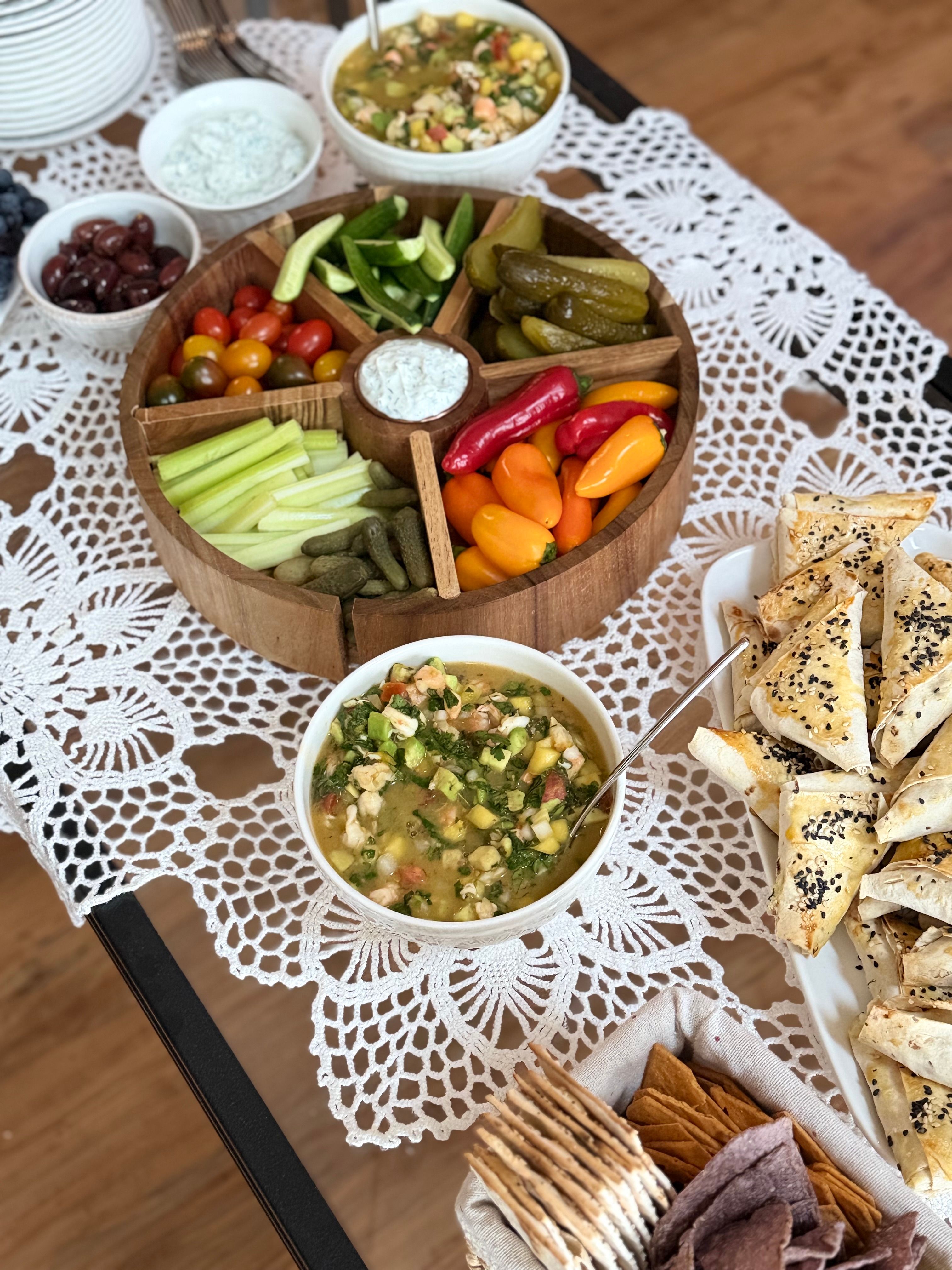 An inviting Mediterranean platter with vegetables, dips, and pastries on a lace tablecloth.