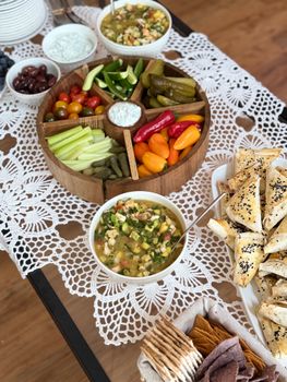 An inviting Mediterranean platter with vegetables, dips, and pastries on a lace tablecloth.