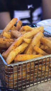 Close-up of crispy, seasoned French fries served in a wire basket at a restaurant.