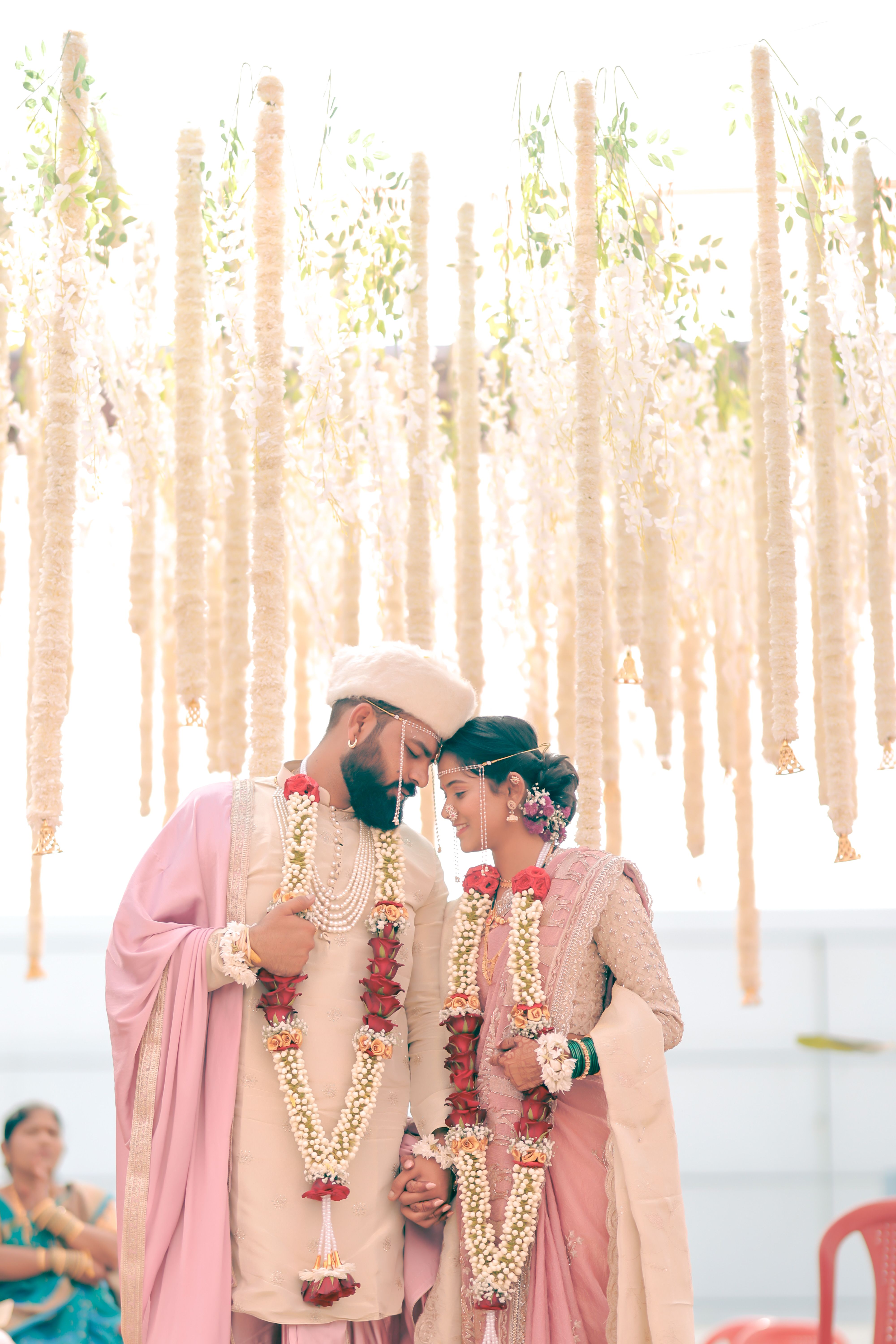 Beautiful Indian couple in pastel attire at their wedding ceremony, adorned with floral garlands.