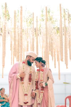 Beautiful Indian couple in pastel attire at their wedding ceremony, adorned with floral garlands.