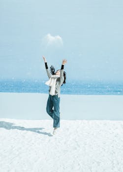 Joyful woman playing in the snow near a blue ocean backdrop, capturing winter fun.