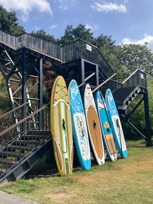 Free Vibrant paddleboards propped against a staircase in a lush outdoor area. Stock Photo