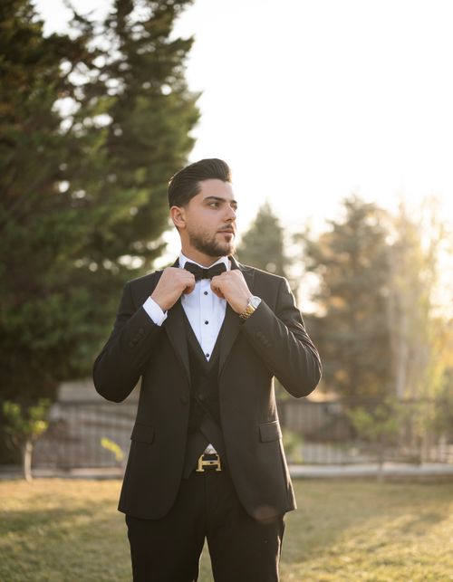 Free A well-dressed man adjusts his bow tie, exuding elegance in a sunlit outdoor setting. Stock Photo