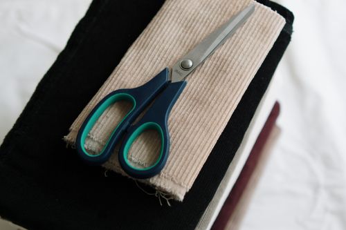 Free Scissors placed on stacked corduroy fabric swatches ideal for sewing projects. Stock Photo
