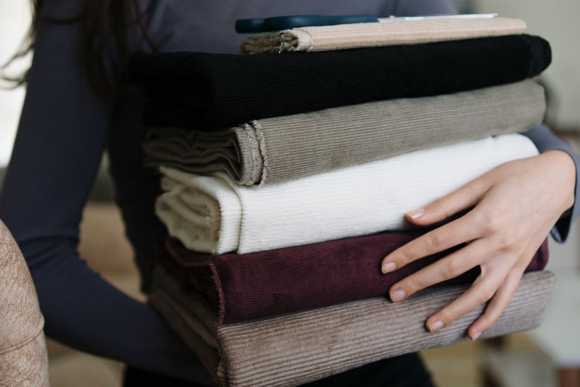 A person carrying a stack of neatly folded fabrics in various colors indoors.