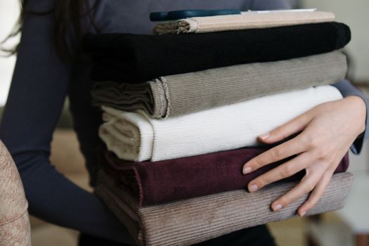 A person carrying a stack of neatly folded fabrics in various colors indoors.