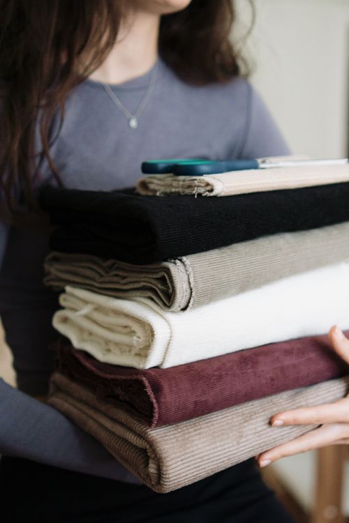 Free A woman holding a stack of neatly folded fabrics in various colors indoors. Stock Photo